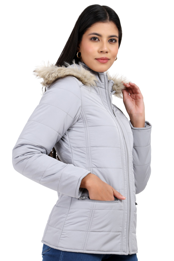 A woman in a standing side pose, wearing Trufit’s grey Matte Quilted Jacket with Horizontal Pockets, zip closure, a removable hood and blue jeans with her right hand in the pocket and holding the hood fur’s trim from her left hand.